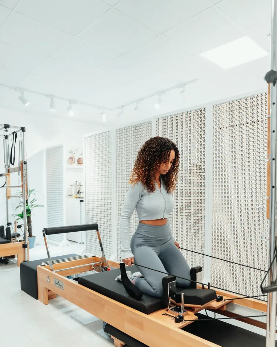 Aluna praticando pilates no reformer em estúdio claro e espaçoso
